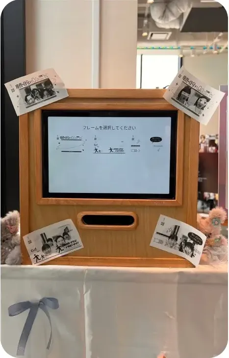 나무 프레임 키오스크 화면에 "프레임을 선택해주세요" 안내와 주변에 붙인 영수증사진 4장, 인형 장식